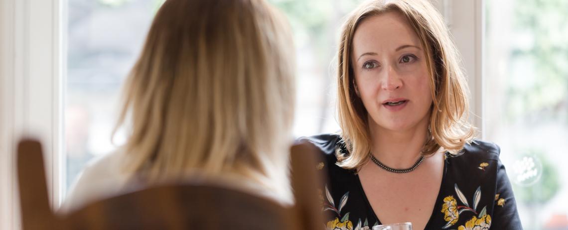 Twee vrouwen in gesprek met raam op achtergrond