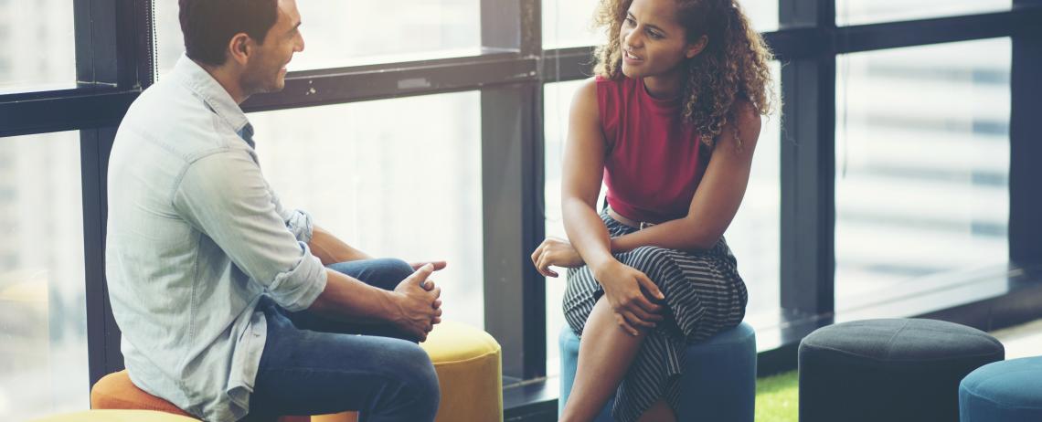 Man en vrouw in gesprek op poef bij raam